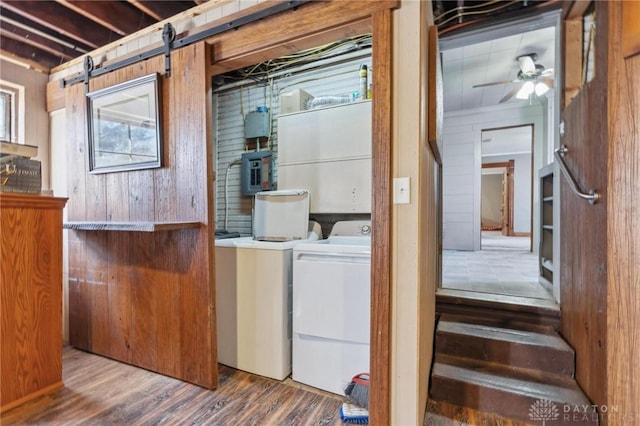 clothes washing area with wood-type flooring, wooden walls, electric panel, ceiling fan, and washing machine and dryer