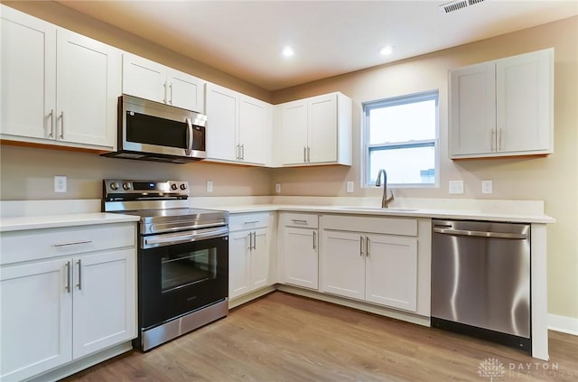 kitchen with stainless steel appliances, sink, white cabinets, and light wood-type flooring