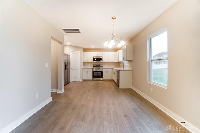 kitchen with stainless steel appliances, light hardwood / wood-style floors, white cabinets, decorative light fixtures, and a chandelier