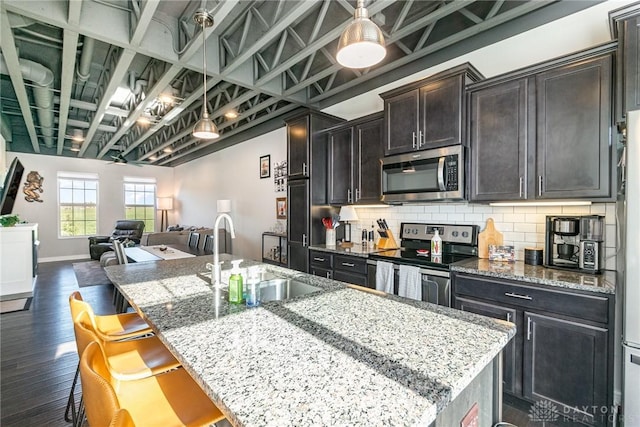 kitchen with sink, a breakfast bar area, light stone counters, an island with sink, and stainless steel appliances