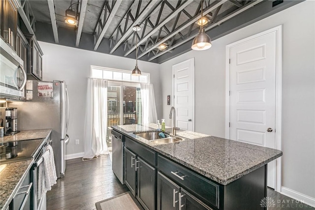 kitchen with dark stone counters, hanging light fixtures, sink, and a center island with sink