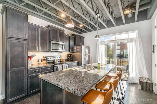 kitchen with dark brown cabinetry, sink, a center island with sink, stone counters, and stainless steel appliances