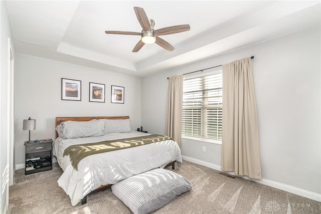 carpeted bedroom with a tray ceiling and ceiling fan