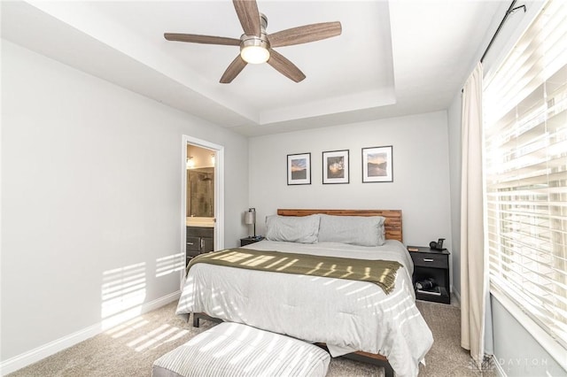 bedroom featuring ceiling fan, ensuite bath, a tray ceiling, and light colored carpet