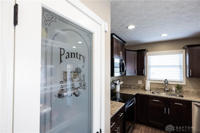 kitchen with sink, light stone counters, dark brown cabinetry, stainless steel appliances, and a textured ceiling