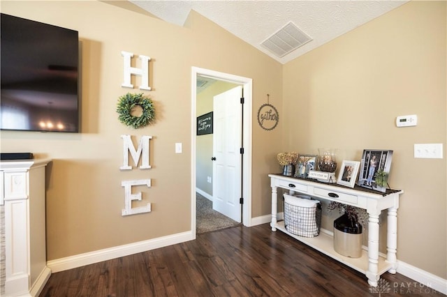 hallway with dark wood-type flooring, vaulted ceiling, and a textured ceiling