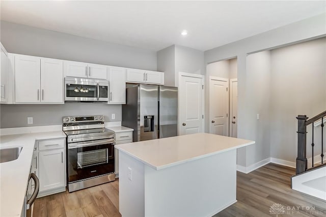 kitchen with light wood-type flooring, stainless steel appliances, white cabinets, and a kitchen island