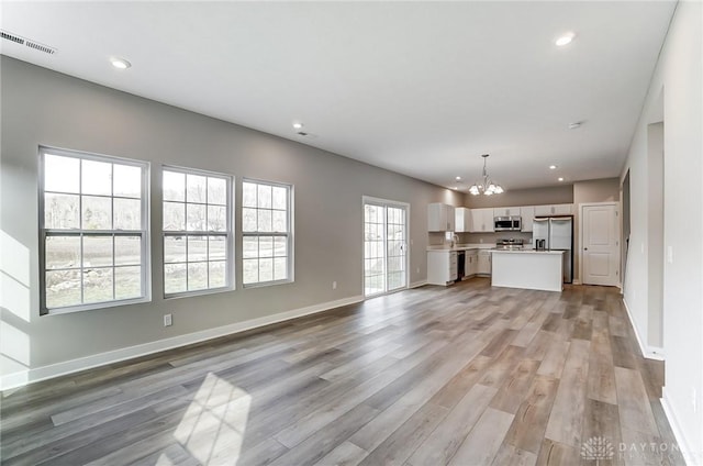 unfurnished living room featuring an inviting chandelier, sink, and light hardwood / wood-style flooring