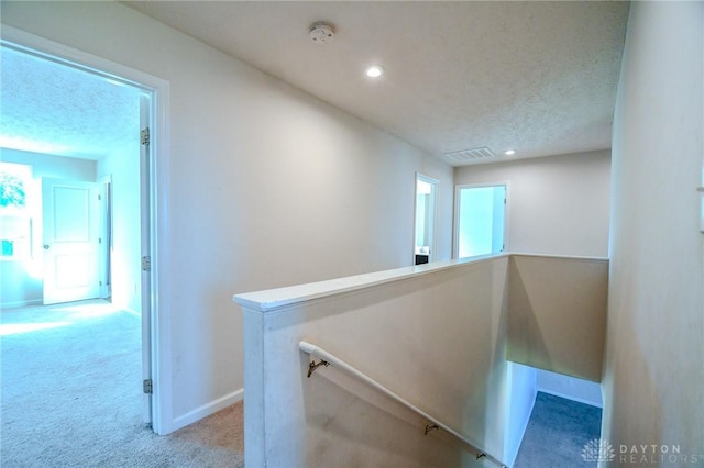 hallway featuring light colored carpet and a textured ceiling