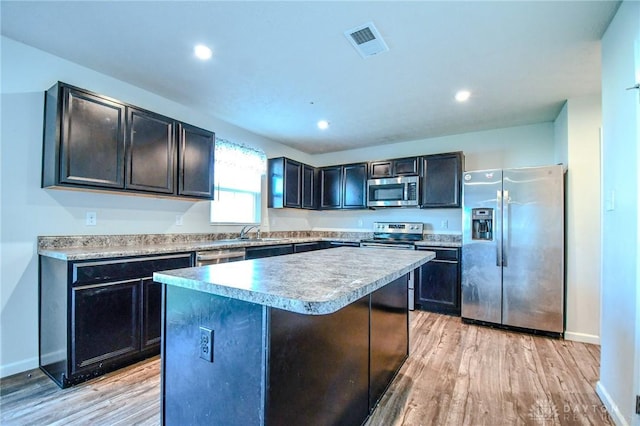 kitchen featuring sink, appliances with stainless steel finishes, a kitchen island, light hardwood / wood-style floors, and a kitchen bar