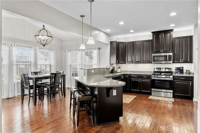 kitchen featuring pendant lighting, dark hardwood / wood-style flooring, a kitchen breakfast bar, kitchen peninsula, and stainless steel appliances