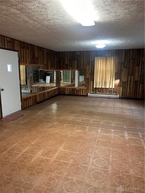 empty room featuring a textured ceiling, wooden walls, and a baseboard radiator