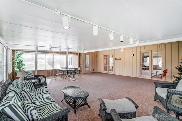 carpeted living room featuring rail lighting and wood walls