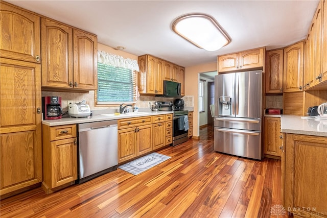kitchen with stainless steel appliances, a sink, light wood-type flooring, and backsplash