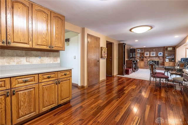 kitchen featuring dark wood-style flooring, light countertops, brown cabinets, and a brick fireplace