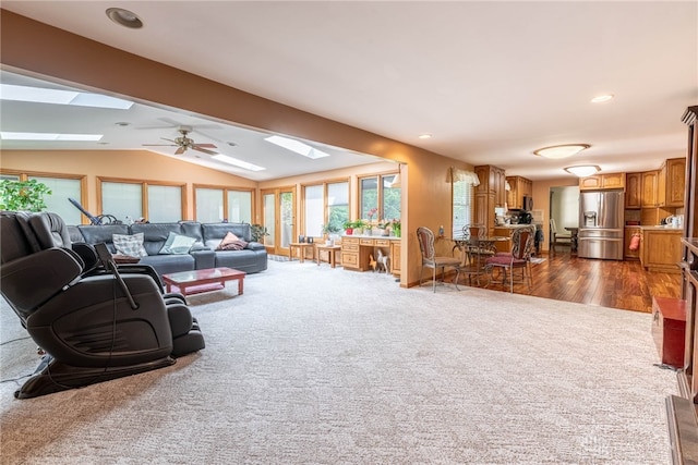 carpeted living room with ceiling fan and vaulted ceiling with skylight