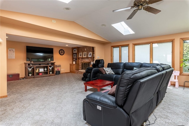 carpeted living room with ceiling fan, vaulted ceiling with skylight, and a fireplace