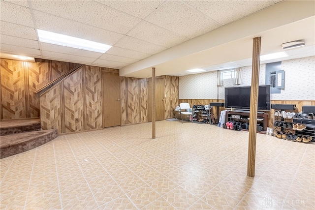 basement featuring a drop ceiling, electric panel, and wood walls