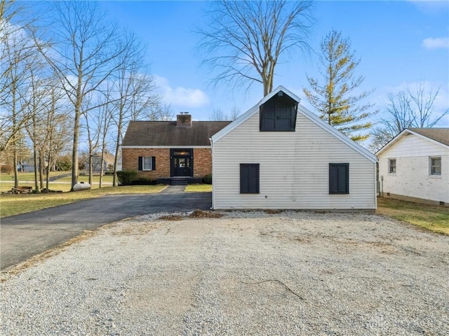 view of front facade featuring driveway, brick siding, and a chimney