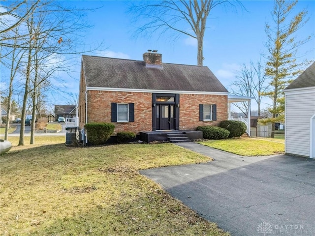 view of front facade featuring brick siding, a chimney, a front lawn, and roof with shingles