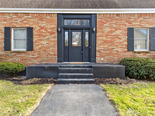 entrance to property featuring brick siding and a shingled roof