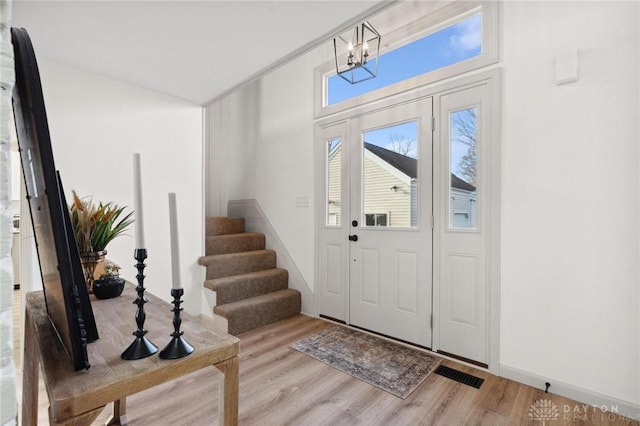 foyer featuring stairs, visible vents, a chandelier, and wood finished floors