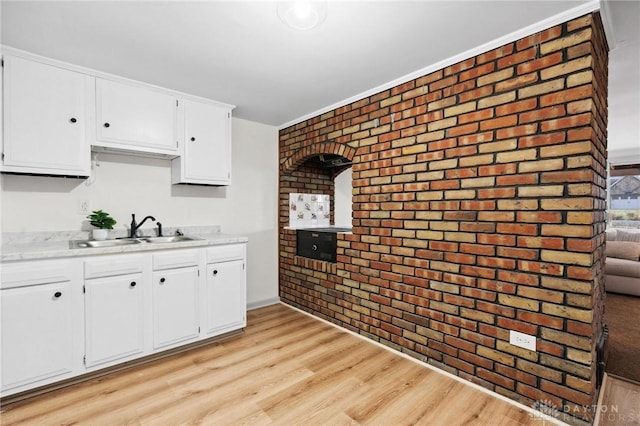 kitchen featuring brick wall, light wood-style flooring, light countertops, white cabinetry, and a sink