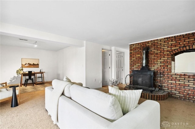 living room featuring light carpet, brick wall, visible vents, and a wood stove