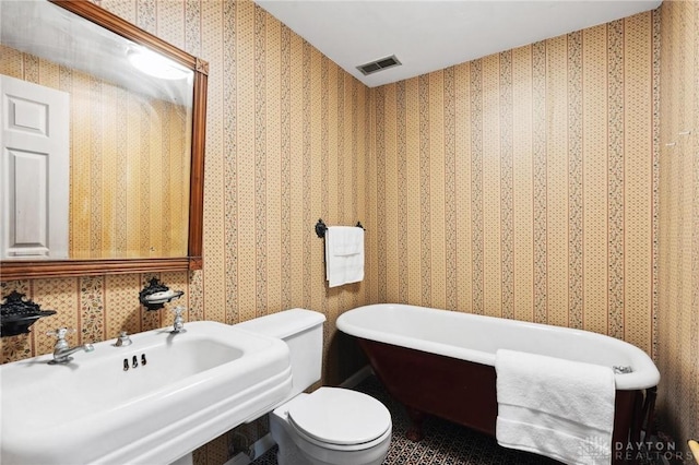 bathroom with toilet, a sink, visible vents, a freestanding bath, and wallpapered walls