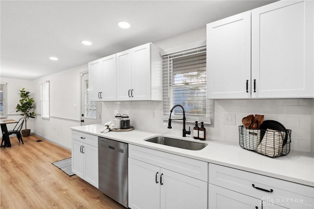 kitchen with sink, white cabinetry, tasteful backsplash, light hardwood / wood-style flooring, and stainless steel dishwasher