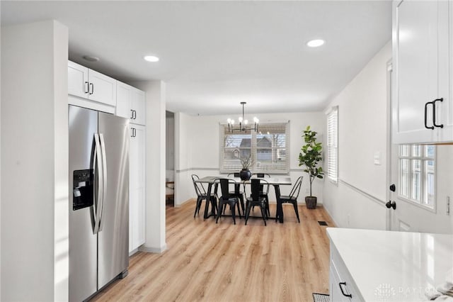 kitchen with stainless steel fridge, white cabinetry, hanging light fixtures, a chandelier, and light wood-type flooring