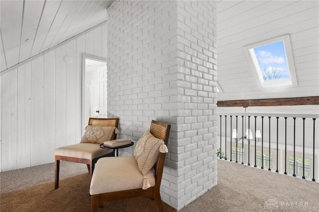 sitting room with wooden walls, carpet flooring, and lofted ceiling with skylight