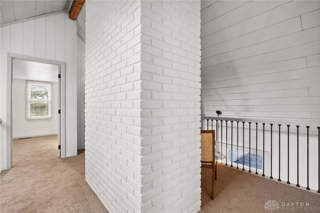 hallway with brick wall, vaulted ceiling with beams, light carpet, and wooden walls