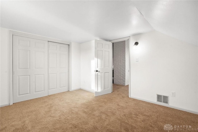 unfurnished bedroom featuring vaulted ceiling, light carpet, and a closet