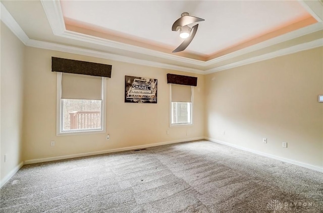 carpeted empty room with a tray ceiling, ornamental molding, and a wealth of natural light