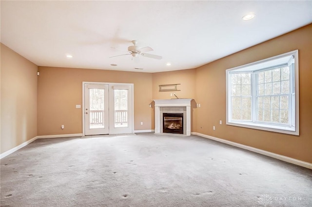 unfurnished living room featuring a tiled fireplace, ceiling fan, and light colored carpet