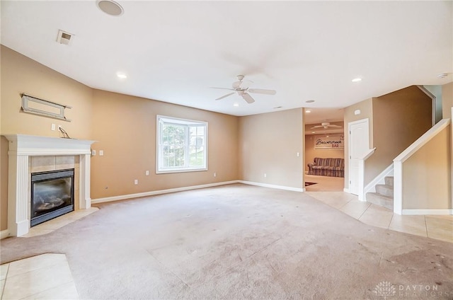 unfurnished living room with a tiled fireplace, light colored carpet, and ceiling fan