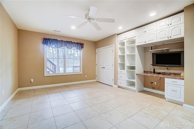 unfurnished living room featuring ceiling fan, built in desk, and light tile patterned floors