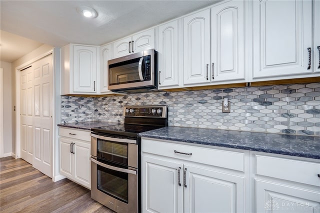 kitchen with white cabinetry, hardwood / wood-style floors, stainless steel appliances, tasteful backsplash, and dark stone counters