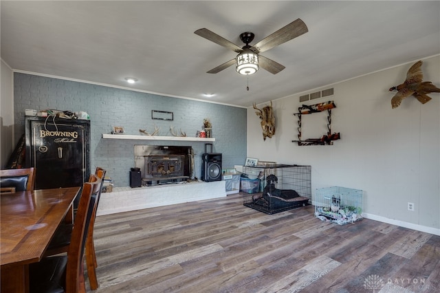 living room with crown molding, ceiling fan, hardwood / wood-style floors, brick wall, and a wood stove