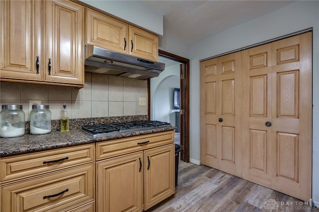 kitchen featuring dark stone countertops, stainless steel gas cooktop, light hardwood / wood-style flooring, and decorative backsplash