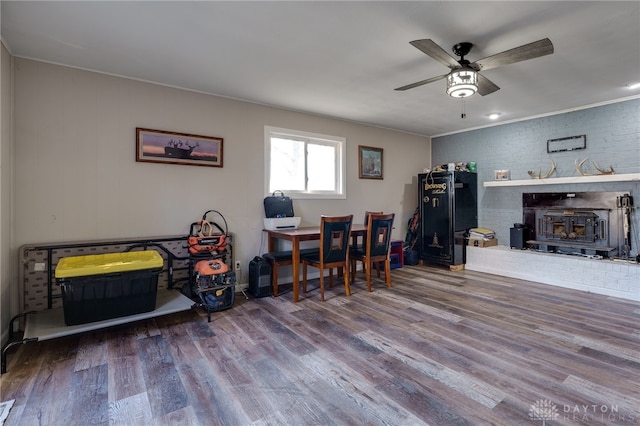 dining area with ceiling fan, wood-type flooring, brick wall, and a wood stove