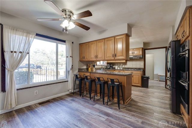 kitchen featuring a breakfast bar, wood-type flooring, sink, decorative backsplash, and kitchen peninsula