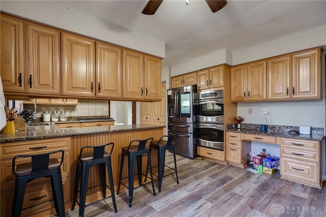 kitchen featuring built in desk, wood-type flooring, a kitchen breakfast bar, dark stone counters, and stainless steel appliances