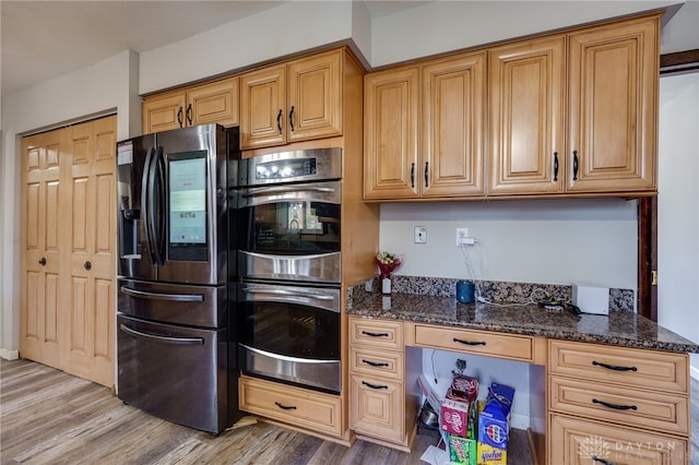 kitchen featuring stainless steel appliances, built in desk, light wood-type flooring, and dark stone countertops