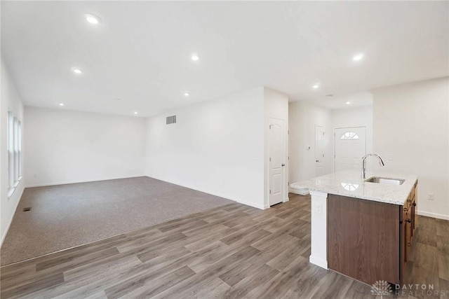 kitchen with sink, light stone countertops, a kitchen island with sink, and hardwood / wood-style floors