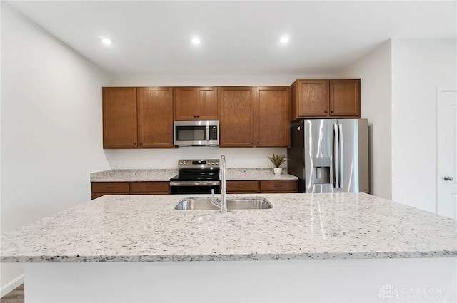 kitchen with stainless steel appliances, a kitchen island with sink, sink, and light stone countertops