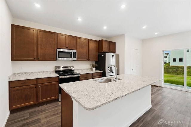 kitchen with dark wood-type flooring, sink, a center island with sink, appliances with stainless steel finishes, and light stone countertops