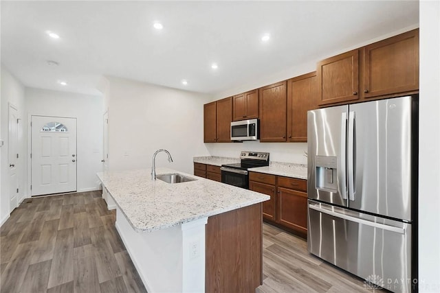 kitchen featuring sink, light stone counters, light wood-type flooring, an island with sink, and stainless steel appliances