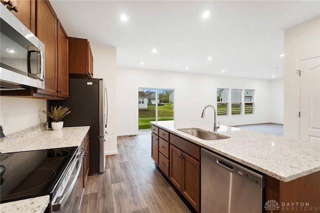 kitchen with sink, wood-type flooring, a center island with sink, appliances with stainless steel finishes, and light stone countertops